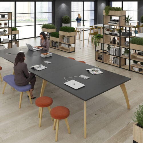 A collaboration table, surrounded by stools and benches, in a large open plan office
