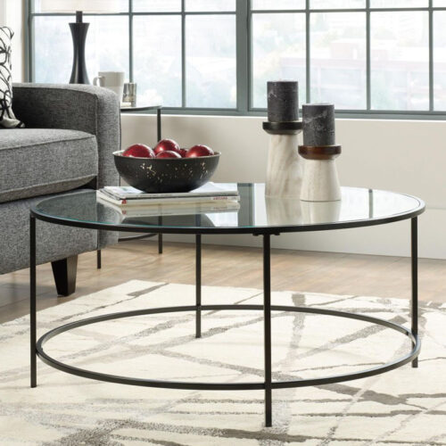 Round glass top coffee table with black frame in front of a grey sofa