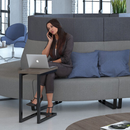 A woman sat on a modular sofa working on a laptop, which is on a laptop table