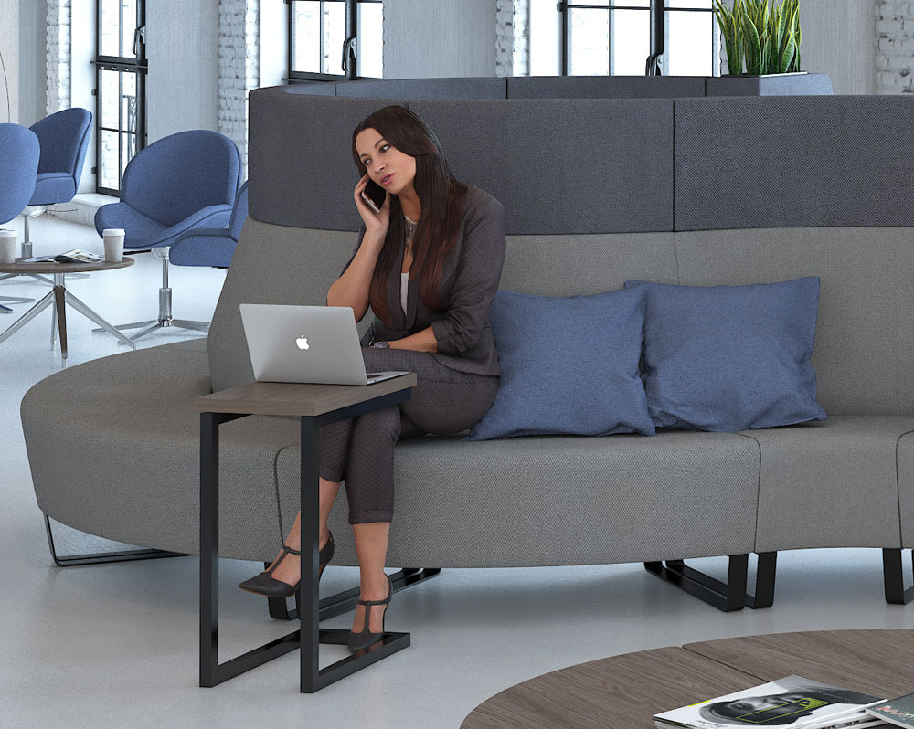 A woman sat on a modular sofa working on a laptop, which is on a laptop table