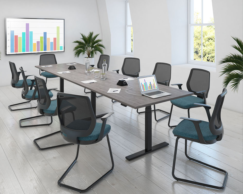 An electric sit stand meeting table surrounded by mesh back meeting chairs